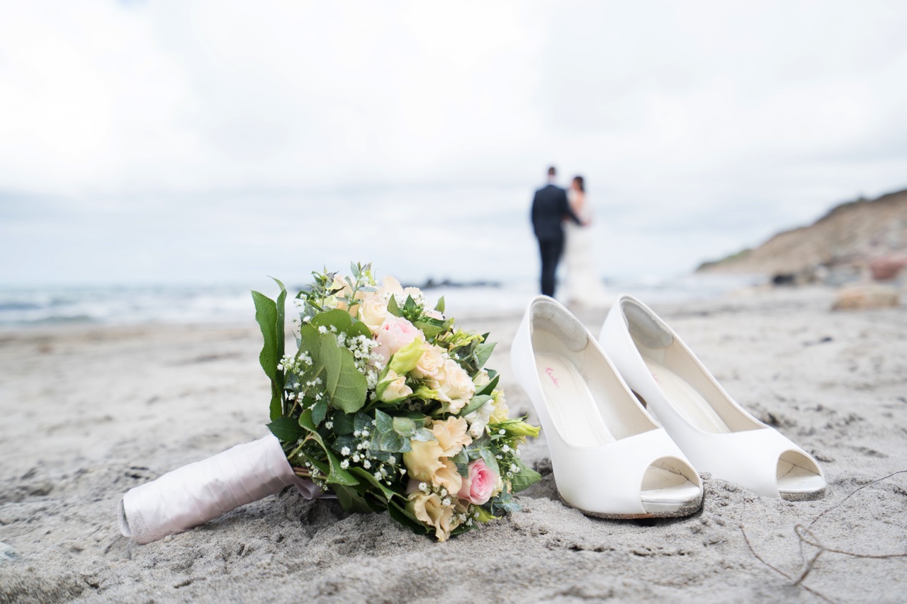 Bryllupbuket og sko på strand under fotografering